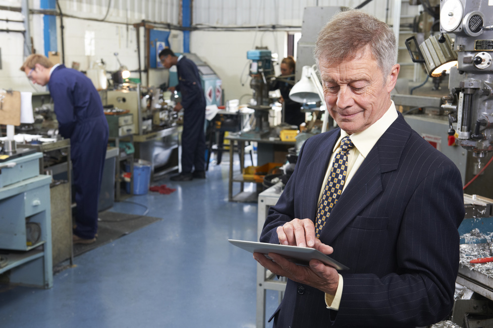 Owner Of Engineering Factory Using Digital Tablet With Staff In Background